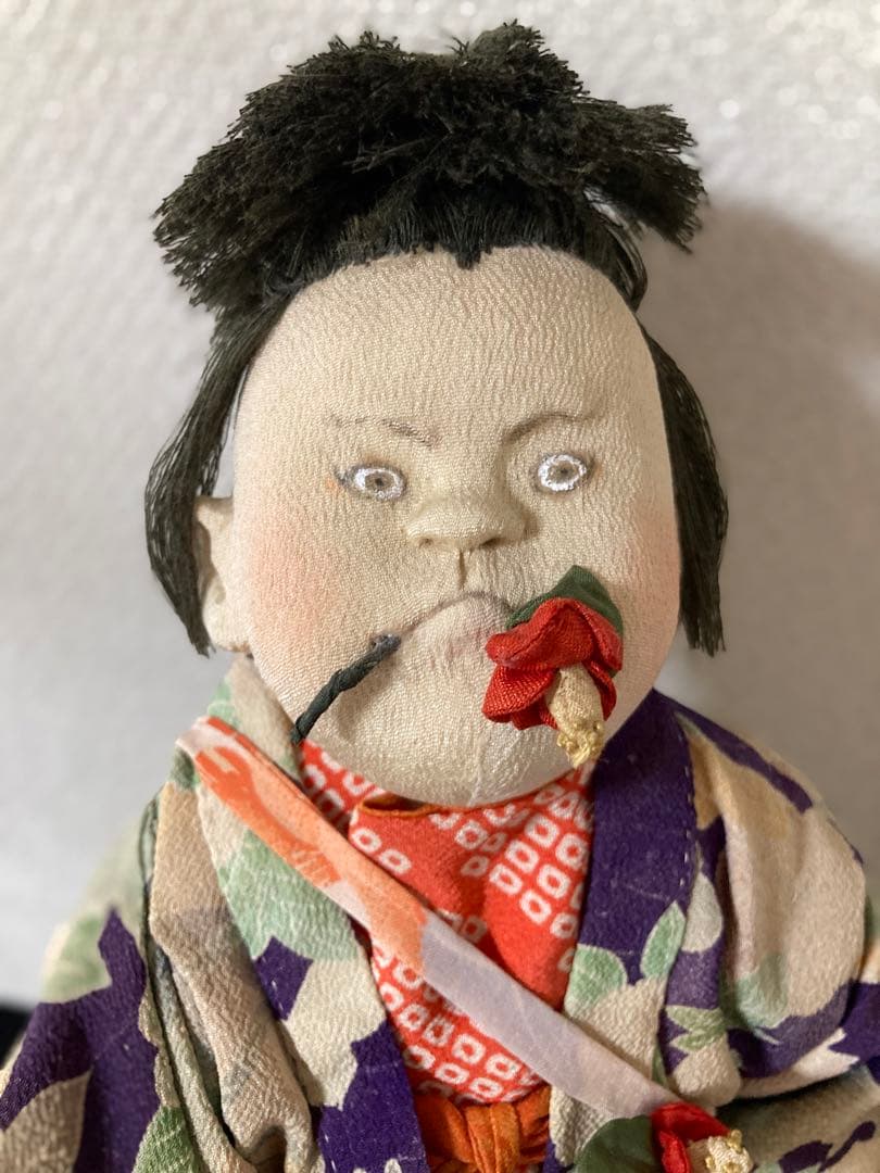 古い縮緬の着物を重ね着、手作りの太鼓を肩からさげています。口に縮緬の椿