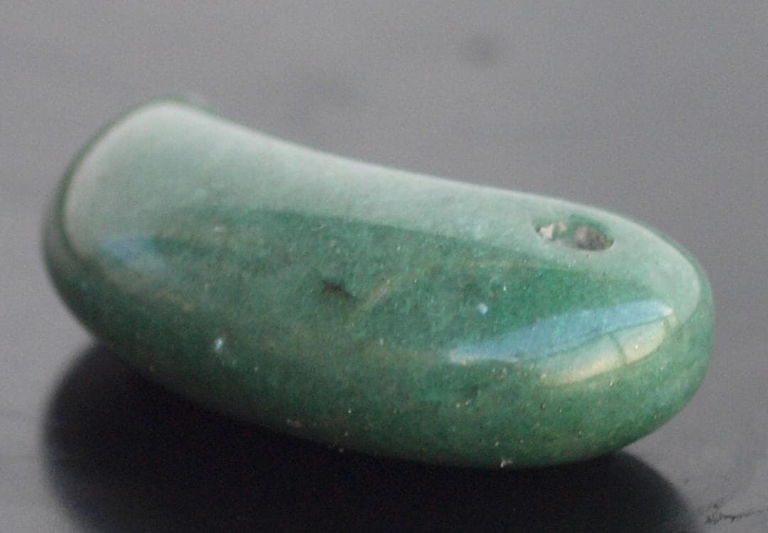 光にかざすと薄緑の細い帯状紋が出現、頭・胴の間には沈線、ずんぐり形の勾玉　沖縄の